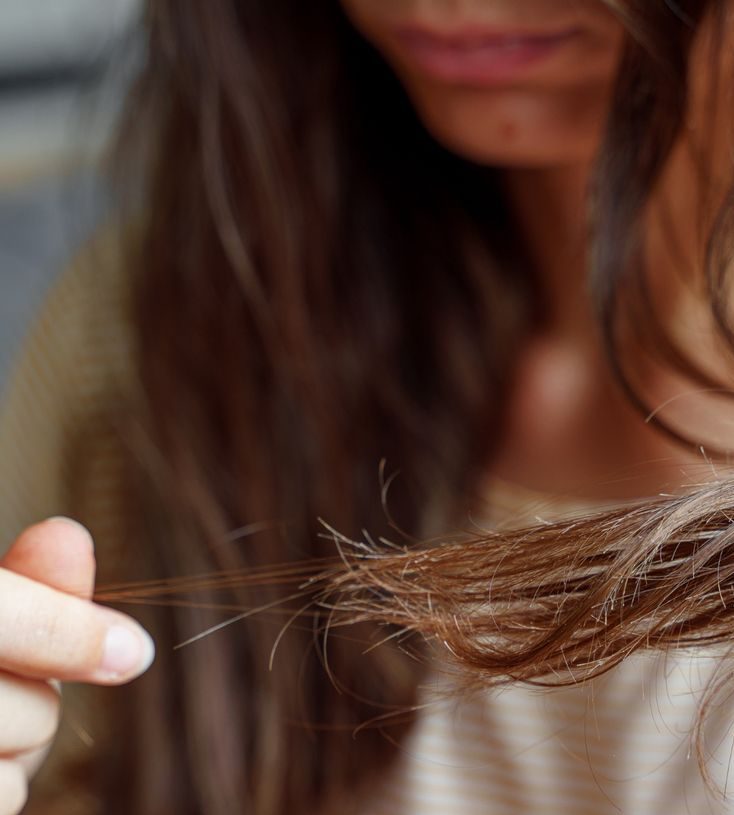 Femme examine ses cheveux abîmés.